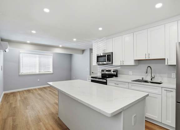 A kitchen with white cabinets and a white island.