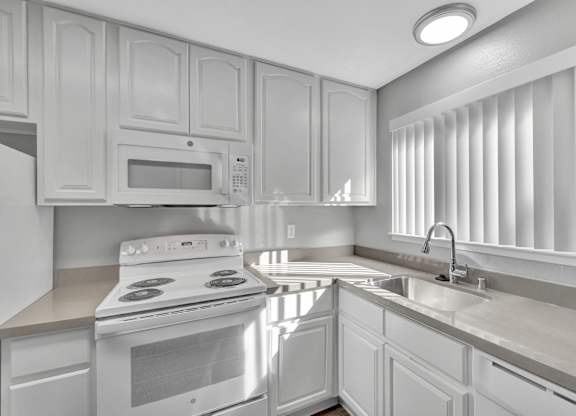 A white kitchen with a stove, microwave, and sink.