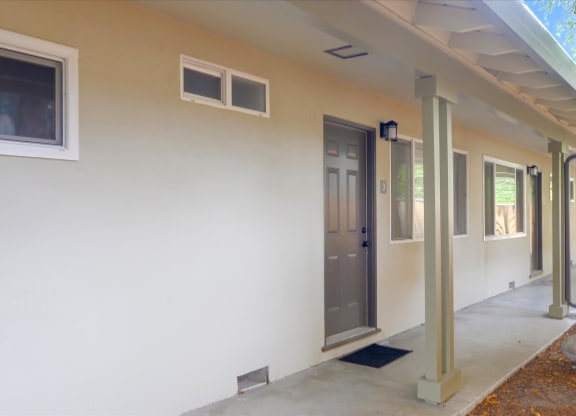A white building with a grey door and a small window on the side.