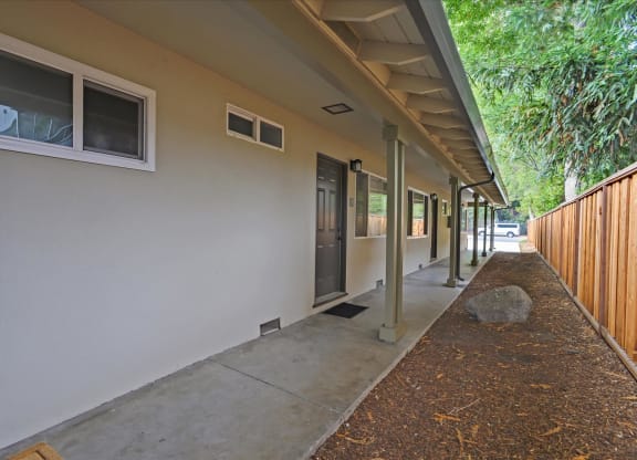 A long concrete walkway leads to a building with a white wall and a window.