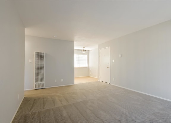 the living room and dining room of an apartment with white walls and wood flooring