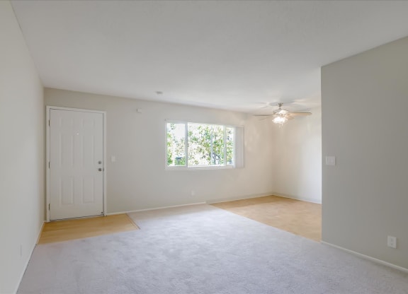 an empty living room with a ceiling fan and a window