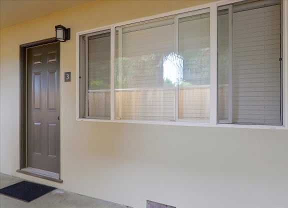 A grey door with a black mat in front of it.