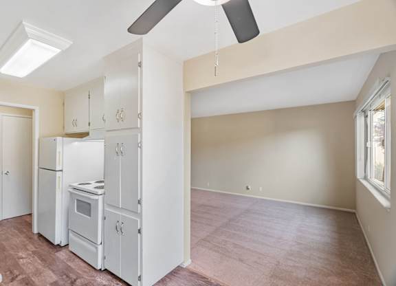 A kitchen with white appliances and a ceiling fan.