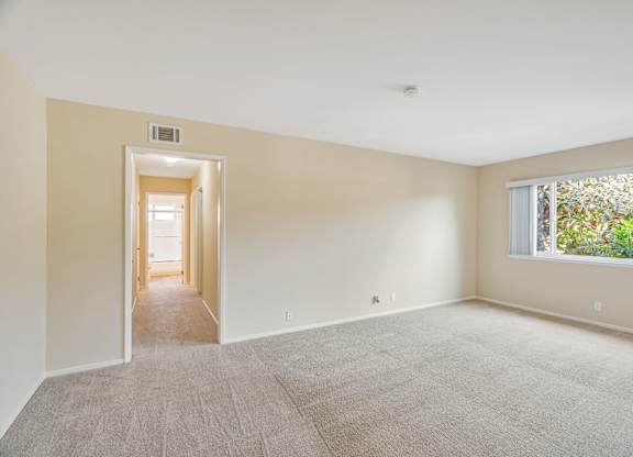 A room with a carpeted floor and a window with a view of trees.