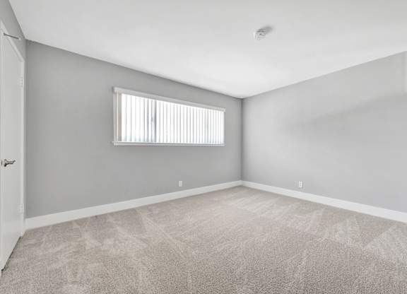 A room with a carpeted floor and a window with blinds.