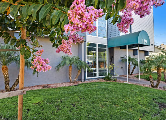 the front of a building with green grass and pink flowers