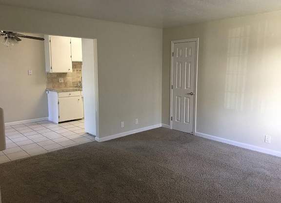 A room with a carpeted floor, a white door, and a white cabinet with a mirror above it.