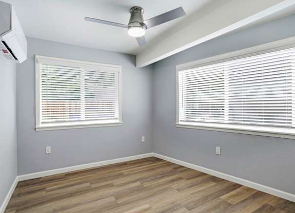 A room with a ceiling fan and two windows with blinds.