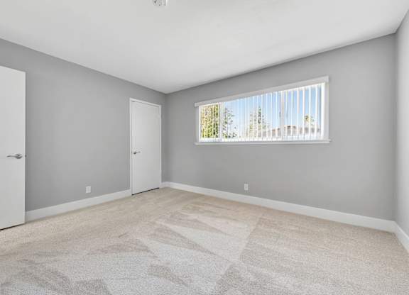 A room with a carpeted floor and a window with blinds.
