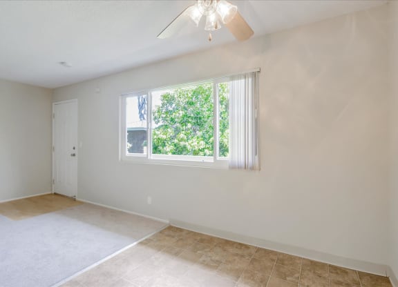 an empty living room with a window and a ceiling fan