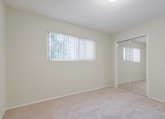 an empty bedroom with a mirrored closet door and a window