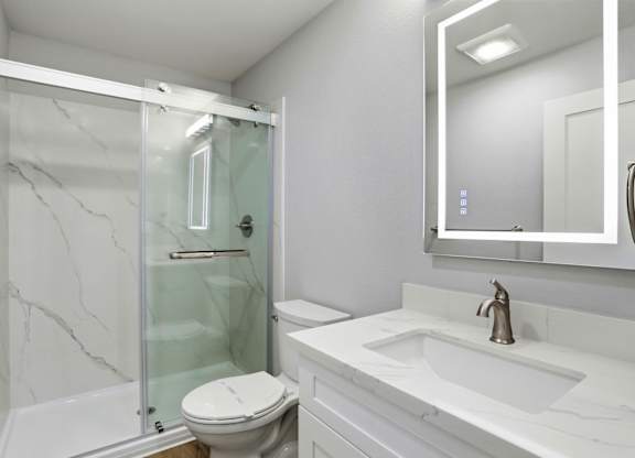 A white bathroom with a marble floor and a glass shower.