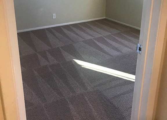A room with a carpeted floor and a window with blinds.