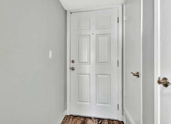 A white door with a brass handle is in a white room.