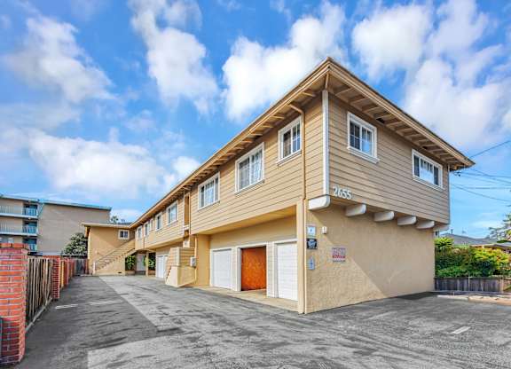 A two-story residential building with a garage is surrounded by a fence and has a clear blue sky above.