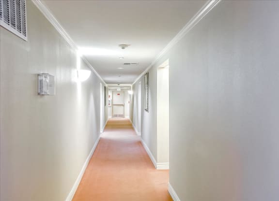 A long hallway with white walls and a brown floor.