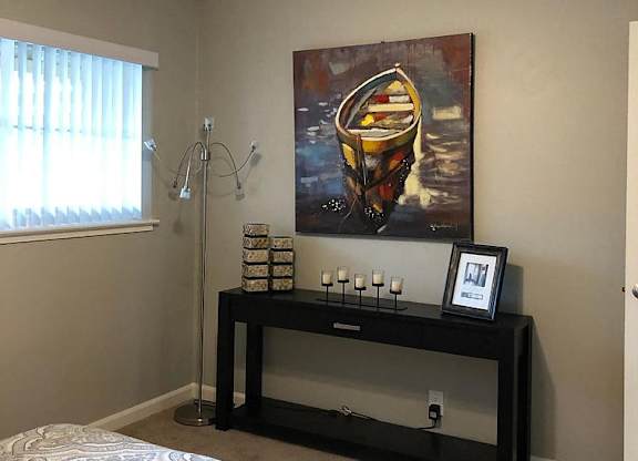 A bedroom with a bed, a ceiling fan, a painting, and a shelf with various items.