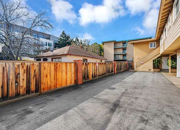 A long driveway with a wooden fence on the left side and a building on the right.