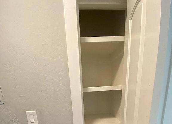 A white closet with shelves and a light switch on the wall.