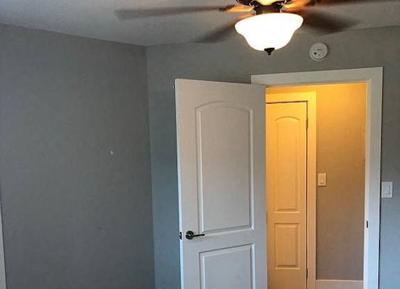 A white door is open to a room with a ceiling fan.