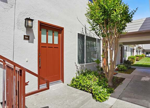 A brown door is on the left side of a white building.