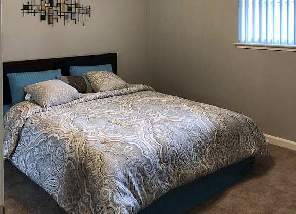 A bedroom with a bed, ceiling fan, and wall art.