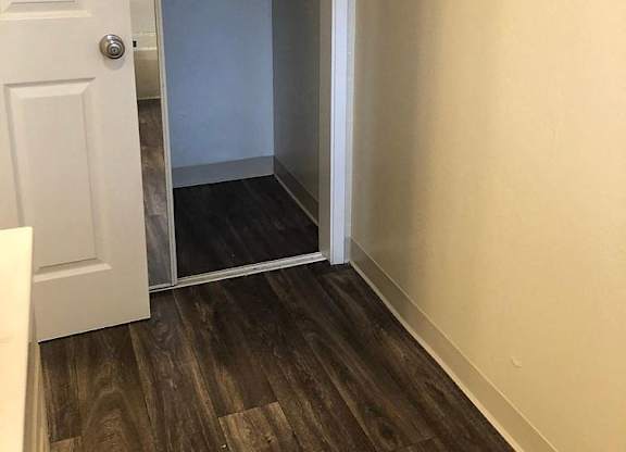 A white door is open to a hallway with wood flooring.