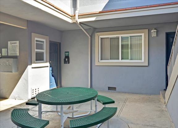 A green table and benches are set up outside a building.