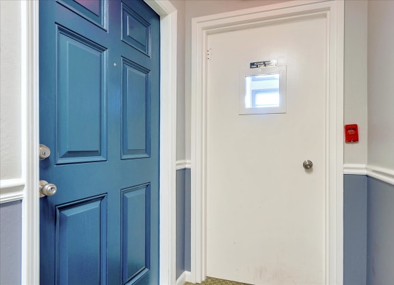 a blue door in a hallway with a white wall and a door with a window