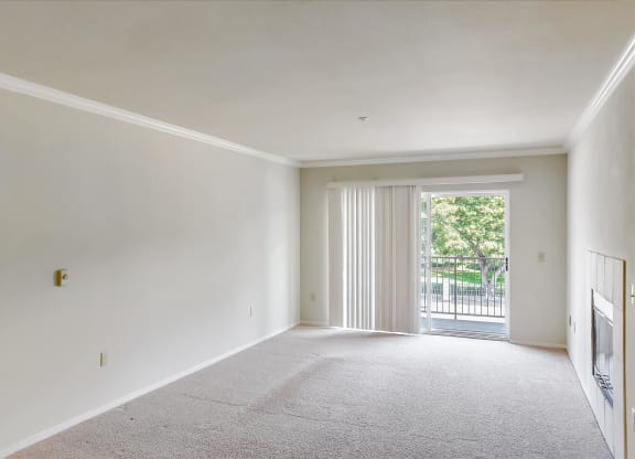 A large, empty room with a carpeted floor and a sliding glass door leading to a balcony.