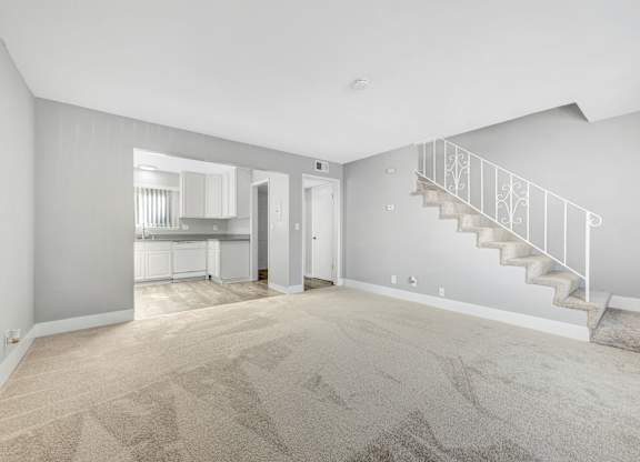 A spacious room with a staircase and a kitchen in the background.