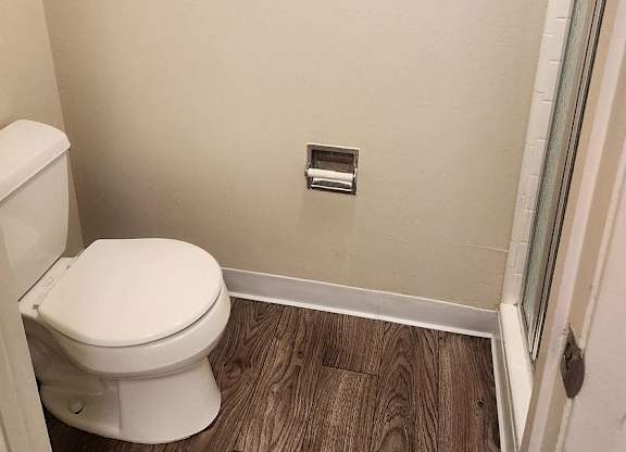 A white toilet in a small bathroom with wood flooring.