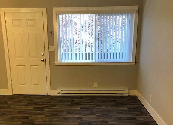 A room with a wooden floor and a window with blinds.