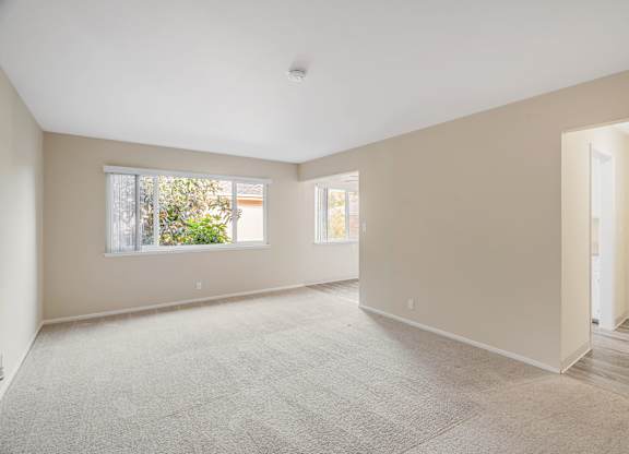 A spacious room with a carpeted floor and two windows.