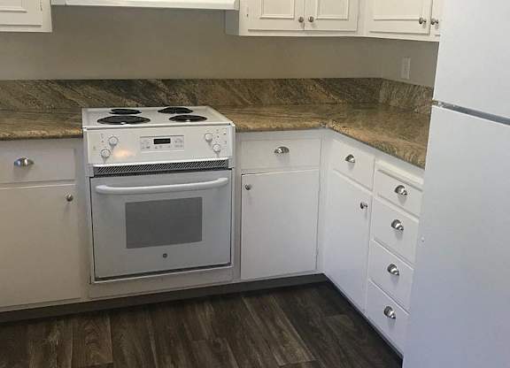 A white stove and refrigerator in a kitchen with wooden floors and white cabinets.