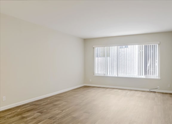 the room of an empty apartment with wood flooring and a window