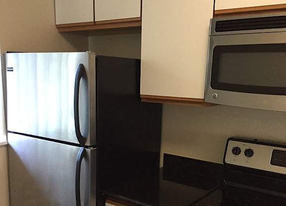 A black refrigerator is in a kitchen with a stove and microwave.