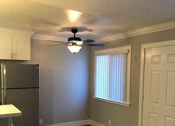 A kitchen with a refrigerator, ceiling fan, and wooden flooring.