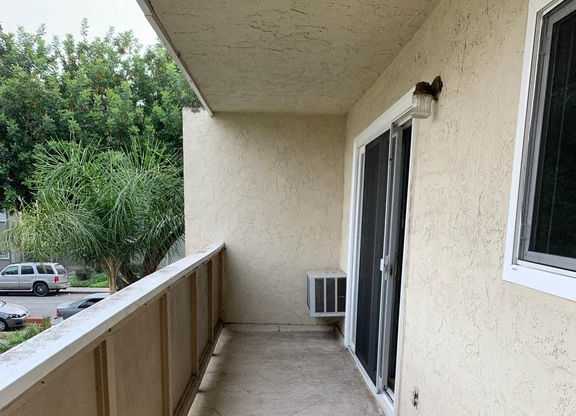 A patio with a tiled floor and a wall with a window and an air conditioning unit.