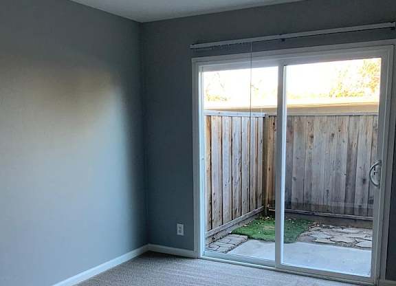 A room with a carpeted floor and a sliding glass door leading to a backyard.