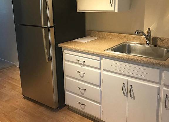 A black refrigerator stands next to a sink in a kitchen.