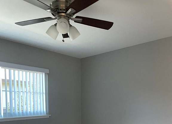 A room with a ceiling fan and a window with blinds.