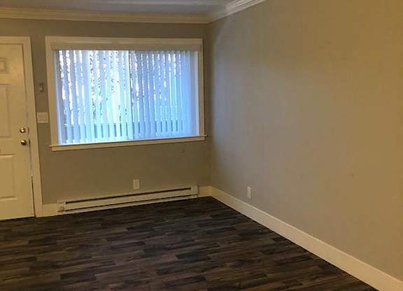 A room with a window covered by white blinds and wooden flooring.
