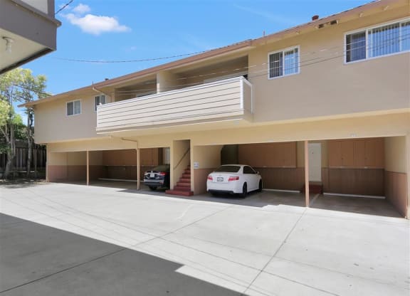A white car is parked in a garage of a two-story apartment building.