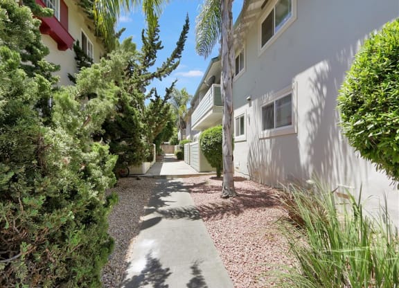 A pathway leads between two buildings with greenery on the sides.