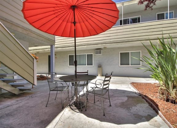 A red umbrella is open over a table with chairs.