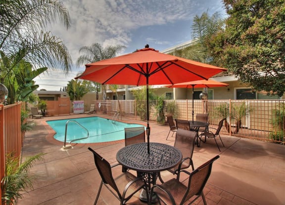 A patio with a table and chairs and a red umbrella.