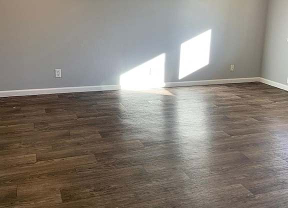 A room with wooden flooring and two windows letting in light.