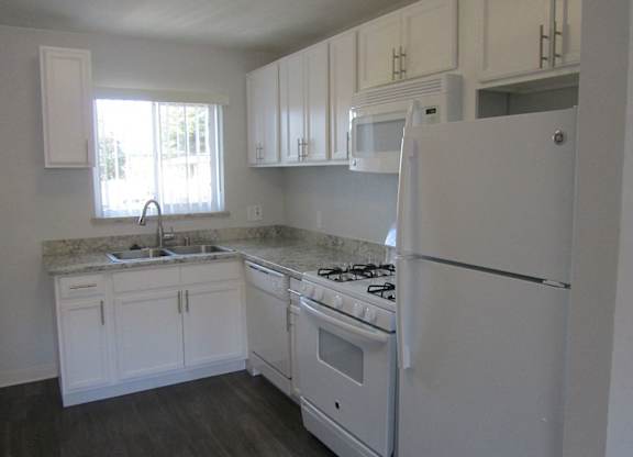 A white kitchen with a stove, sink, and cabinets.